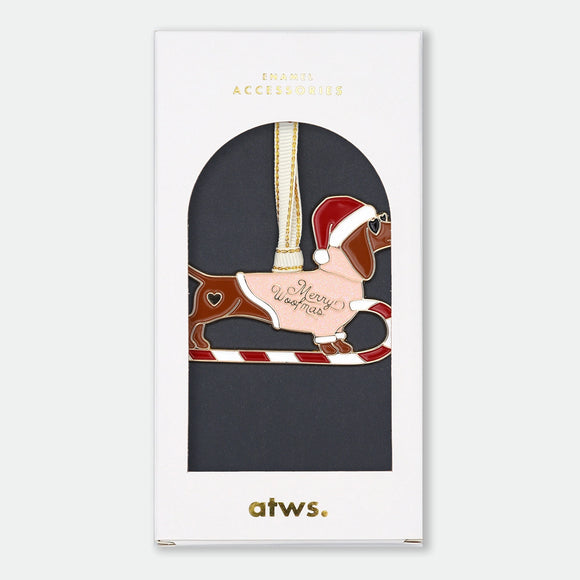 Gold-tone enamel Christmas ornament of a dachshund shaped like a candy cane sleigh, wearing a Santa hat, with a heart detail and text reading "Merry Woofmas"
