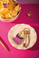 Crunchiest potato chip enamel keychain on a ceramic dish, next to a bowl of chips with a matching potato chip enamel pin