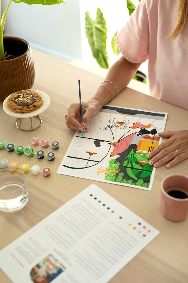 Dog Sitter paint by numbers in progress on a table with 15 paint pots, a glass of water, coffee and the color guide