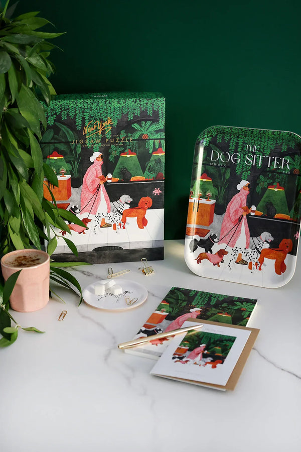 The Dog Sitter New York puzzle and matching notebook displayed on a white marble desk with coffee and stationery accessories – illustrated by All the Ways to Say.