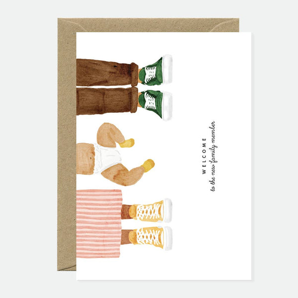 Greeting card with an illustration of a baby wearing sneakers and a text that reads 'Welcome Baby Family Member'. The card has a natural white background and a recycled brown envelope.