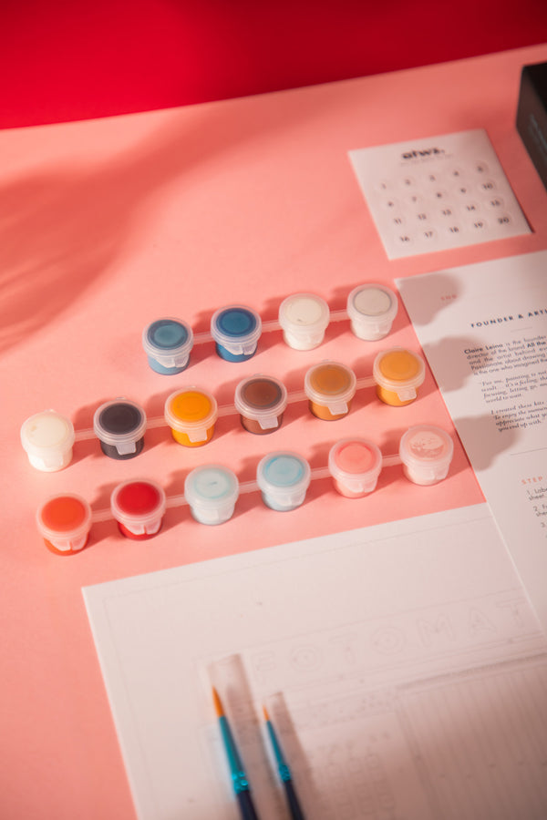 16 acrylic paint pots from the Fotomatic paint by numbers kit in red, blue, orange and brown, next to the numbered canvas