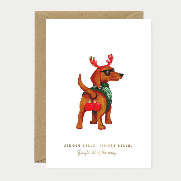 Illustrated Christmas card of a dachshund in reindeer antlers and sunglasses wearing a green sweater with red ornaments, gold foil text reading "Jingle bells, jingle bells, Jingle all of the way..."