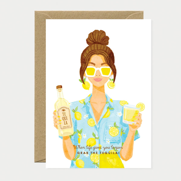 Illustrated greeting card of a woman wearing a lemon-print shirt and yellow sunglasses, with lemon slice earrings, holding a bottle of tequila and a glass of tequila with a lemon slice, text reading "When life gives you lemon, grab the tequila!"