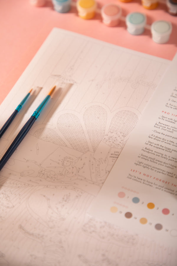 Two paintbrushes on the numbered Life Without Humans canvas, with the scalloped headboard outline and color chart