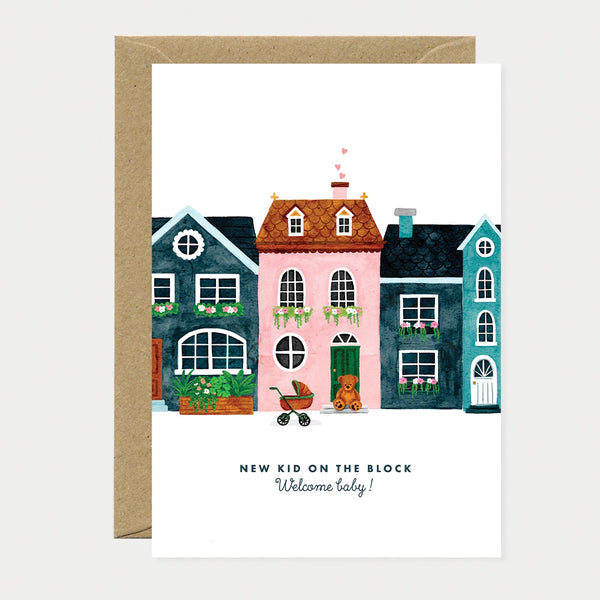 Illustrated greeting card of a row of townhouses with a pink house in the center, hearts rising from the chimney, a stroller and teddy bear by the front door, text reading "New Kid on the Block, Welcome baby!"