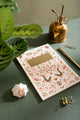 Pink Croco Notebook A5 - Lifestyle view on a dark green desk with a gold water sprayer and pen.