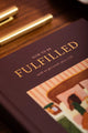 How to be fulfilled Hardcover Notebook A5 - Close-up of the gold foil title and textured burgundy cover.