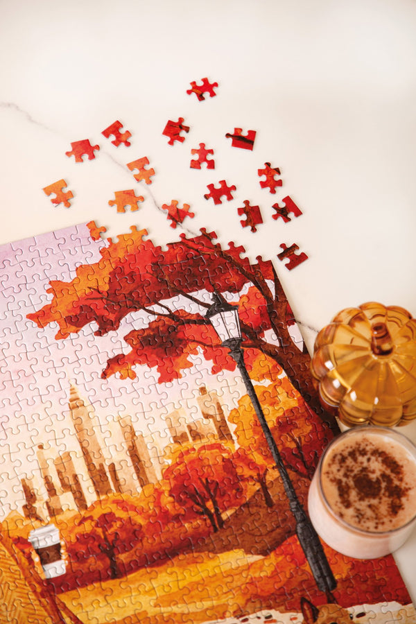October Walks 1000 piece puzzle in progress, red autumn trees, a street lamp and the New York skyline, with a pumpkin jar and a latte
