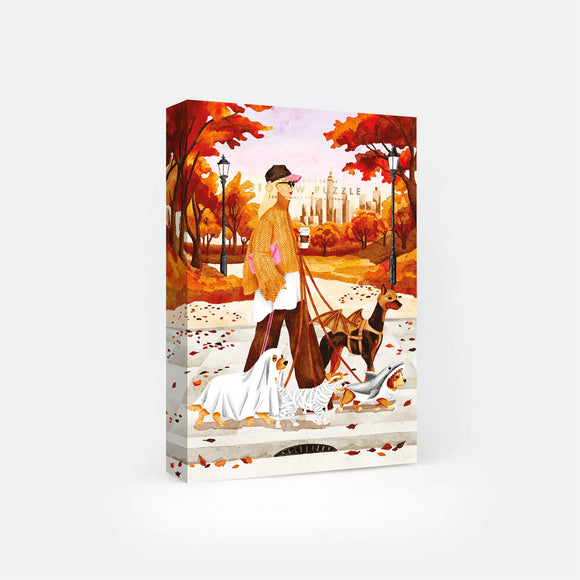 October Walks 1000-piece jigsaw puzzle box by All The Ways To Say, illustration of a woman walking three dogs dressed as a ghost, mummy and shark through an autumn park with a city skyline, text reads "1000 pieces / 500mm x 700mm".