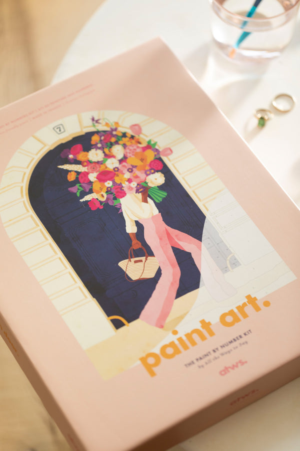 Parisian Door paint by numbers box: woman carrying a giant flower bouquet in front of a navy Paris door