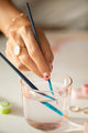 Hand rinsing a paintbrush in a pink glass of water while painting the Parisian Door paint by numbers kit
