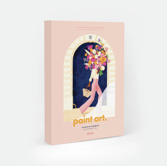 Parisian Door paint by numbers kit box by All The Ways To Say, illustration of a woman walking away from a blue Parisian doorway numbered 7, carrying a large bouquet of flowers and a woven basket, "paint art. The Paint By Number Kit by All The Ways To Say"