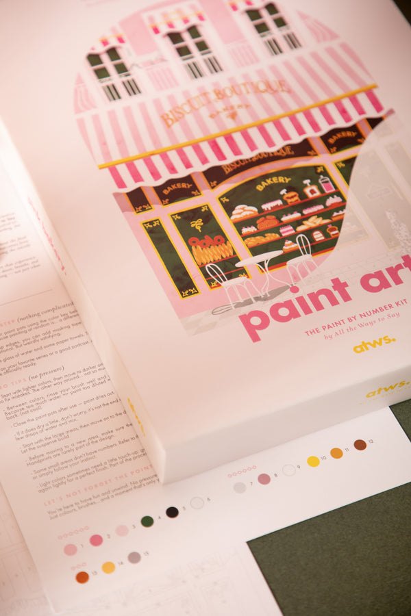 Pink Bakery paint by numbers kit box showing a pink striped Parisian bakery front, with the numbered color chart