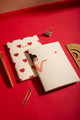 Bisou Pocket Notebook A6 DUO - Lifestyle view on a red desk with gold stationery.