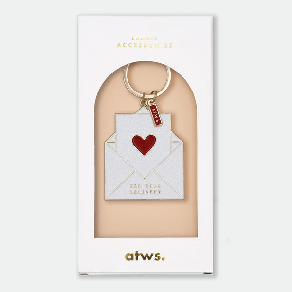 Enamel and metal keychain shaped like an open white envelope with a red heart inside, gold text reading "Red flag delivery," gold-tone ring and "ATWS" charm