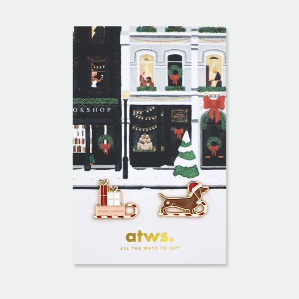 Set of two enamel pins: a sleigh loaded with wrapped presents, and a dachshund wearing a Santa hat riding a candy cane sleigh