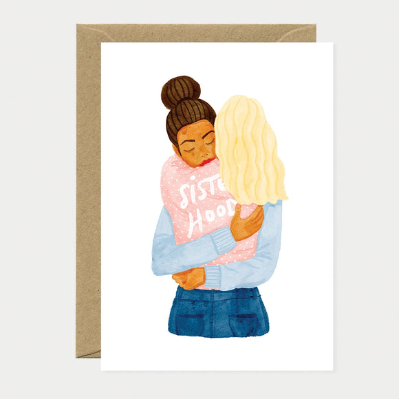 Illustrated greeting card of two women embracing, one wearing a pink sweater with "Sisterhood" written on it and her eyes closed
