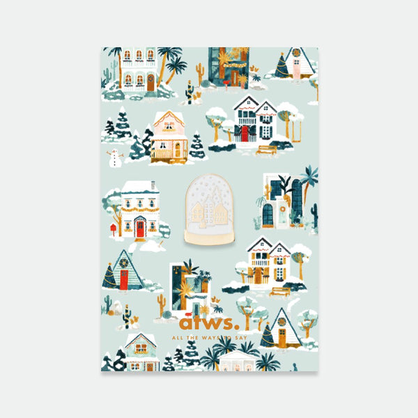 Chic Snowball enamel pin by All the Ways to Say featuring golden snow globe design with small winter village on illustrated pastel background with houses and snow.