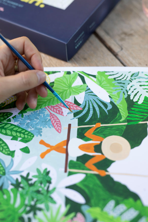 Close-up of a brush painting pink and green tropical leaves around the woman on a swing, Swing paint by numbers kit