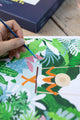 Close-up of a brush painting pink and green tropical leaves around the woman on a swing, Swing paint by numbers kit