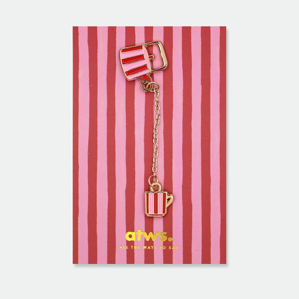 Enamel pin of a red and pink striped teapot connected by a gold chain to a matching striped teacup