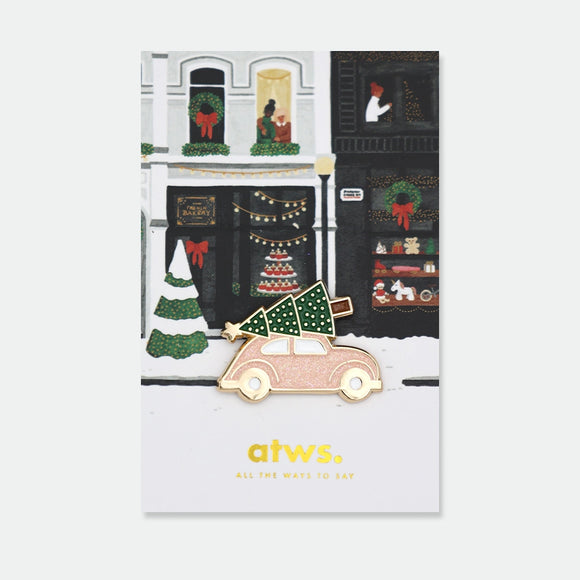 Enamel pin of a pink car with a Christmas tree and gold star strapped to the roof