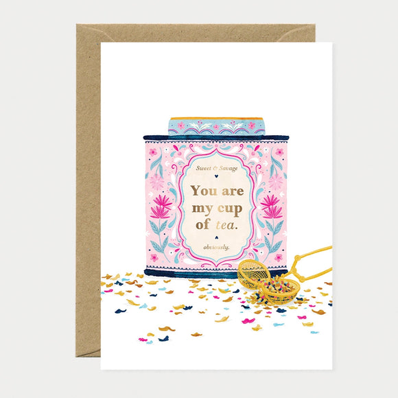 Illustrated greeting card of a pink and gold floral tea tin with a gold foil label reading "Sweet & Savage, You are my cup of tea, obviously," surrounded by loose tea leaves and confetti